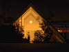 Carrie Graber's artwork of a lady outside the door of an A-Frame house at night. The ladies dress is black and deep V back