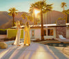 Carrie Graber's artwork of two ladies by the pool at sunset in Palm Springs looking into the mountain. One is in a yellow dress, one is in a white jumpsuit. 